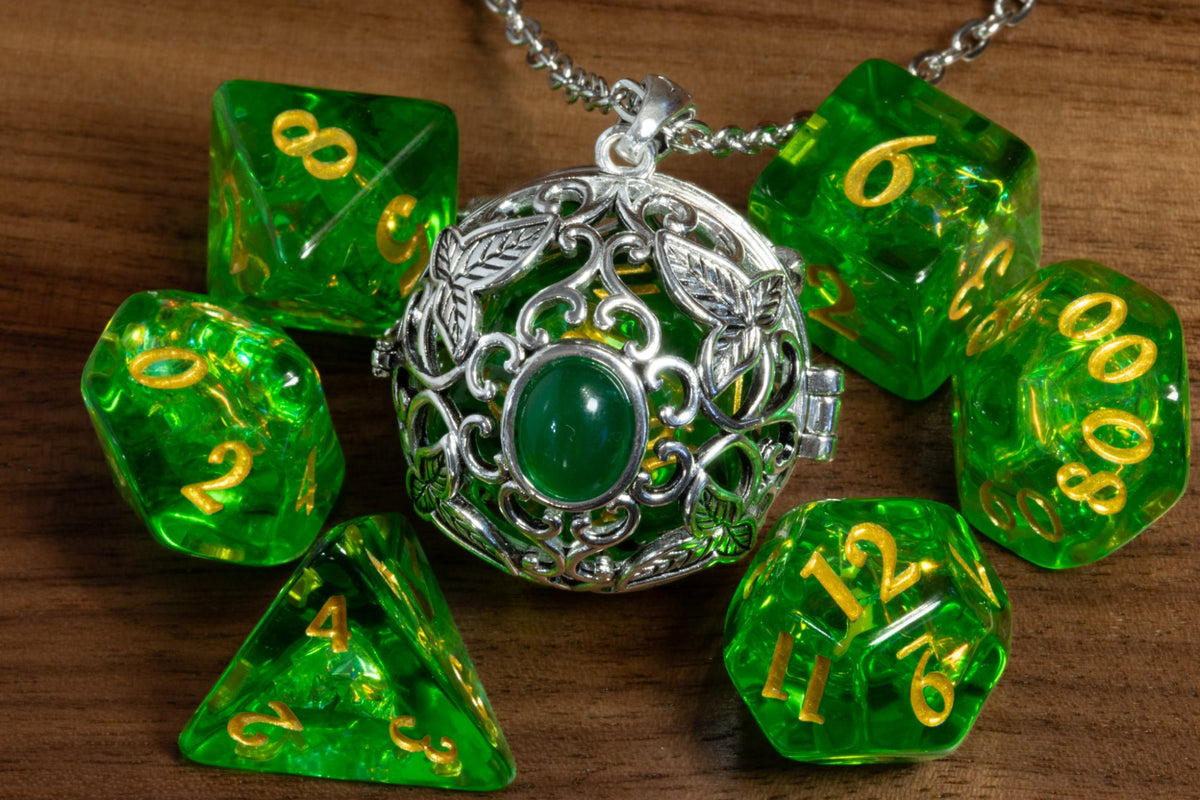 Elvish leaves pendant in a silver finish with a green cabochon, holding a green D20, beside a green holographic dice set on wood