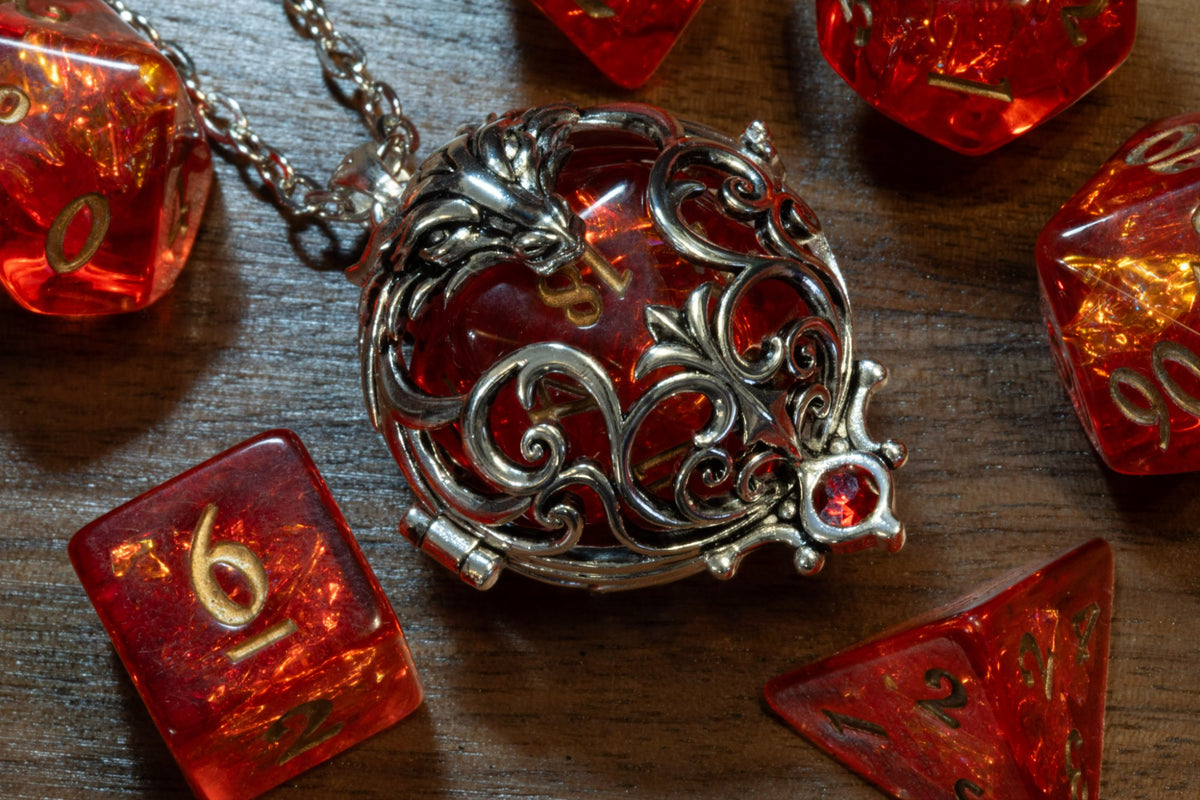 Close-up of the dragon pendant in a silver finish, hinge and openwork scrolls over a red D20, red crystal at the base