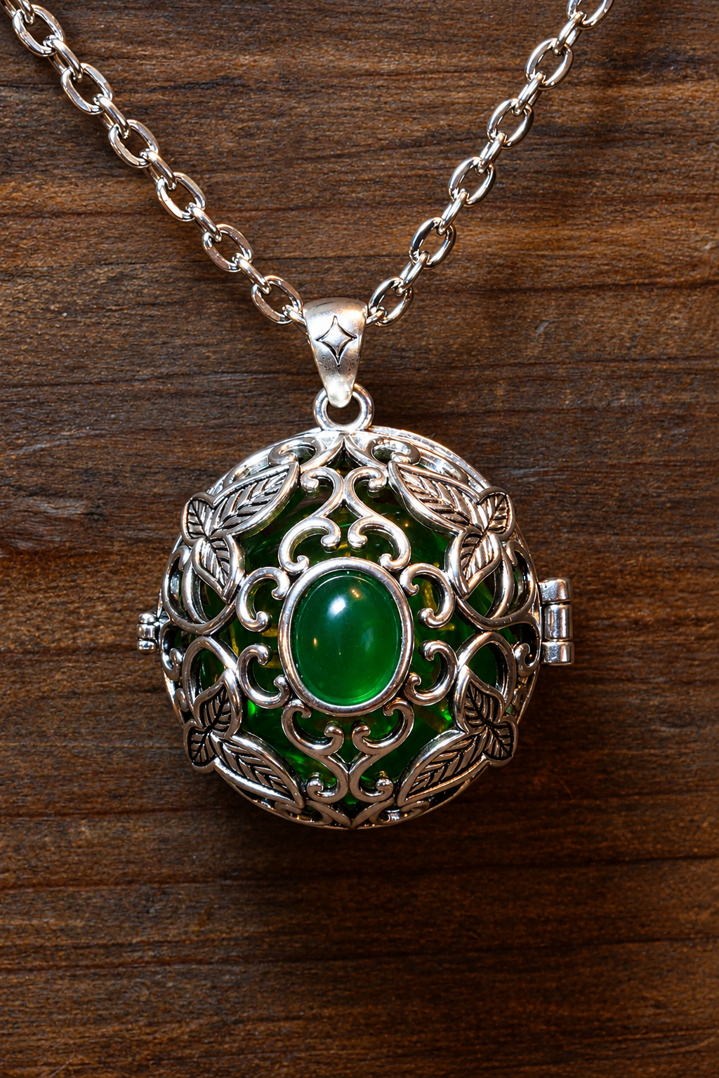 Elvish leaves pendant in a silver finish with a green cabochon, closed, holding a green D20, hanging on its chain against wood